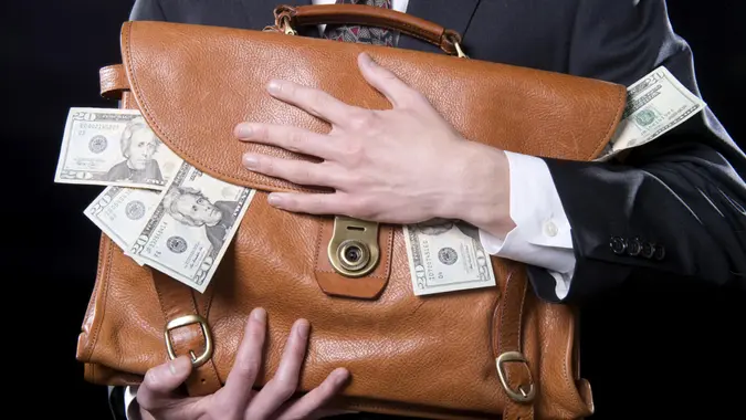 Closeup of man holding briefcase with money spilling out close to his chest.