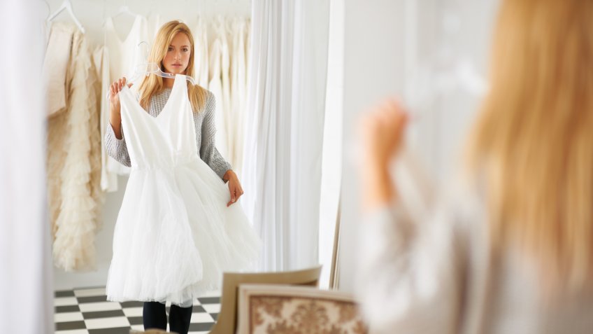 A young bride looking at her reflection in a mirror while choosing a dress.