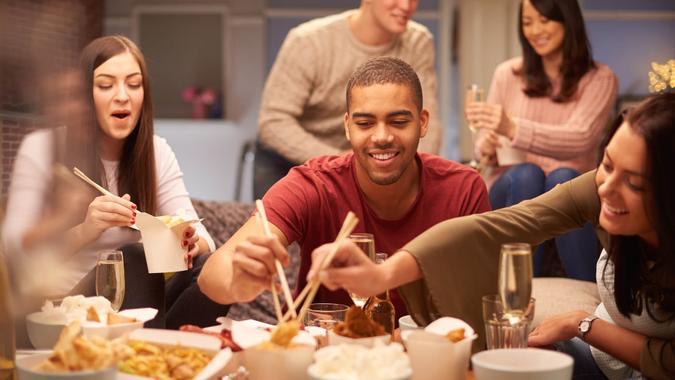 Stock, shares, NASDAQ, S&P 500, money, a group of young friends sit on the sofa and share a chinese take away meal , chatting and laughing with each other as they use their chopsticks to eat .