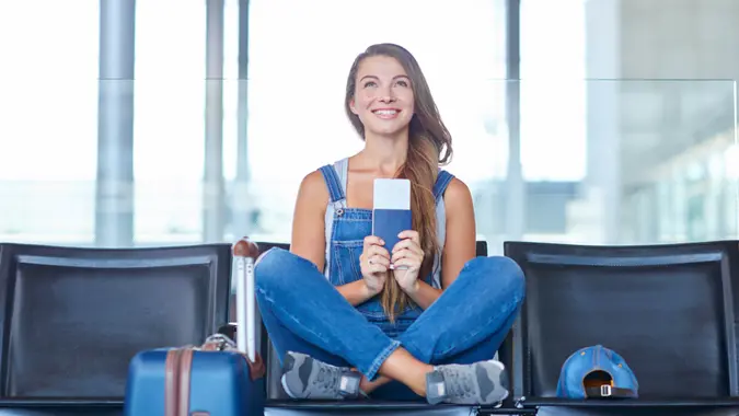 Shot of a young woman holding her passport and ticket while sitting on a chair in an airport departure lounge