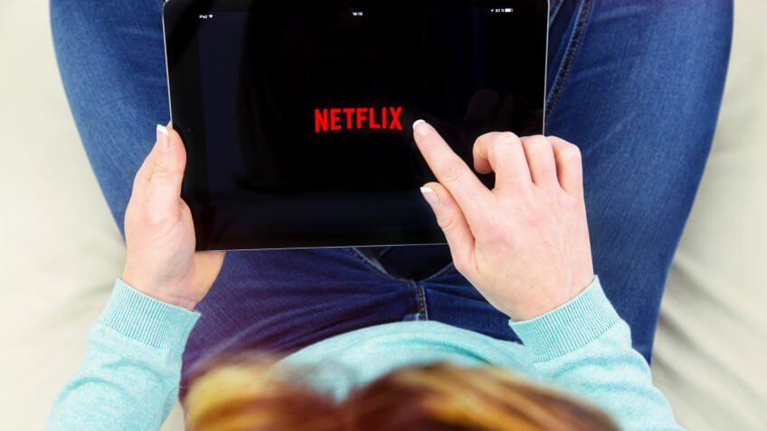 Stock, shares, NASDAQ, S&P 500, money, Benon, France - January 21, 2018: woman sitting cross-legged on her couch and using her touch pad to connect to the Netflix app.