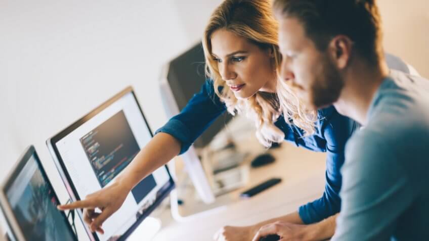 Two colleagues reviewing work on several computer monitors