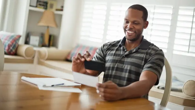 Mid adult man using mobile phone to deposit, fees, America, money, payment, avoid fees, bills, debt