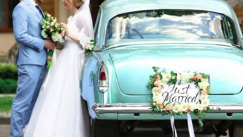 Happy wedding couple near decorated car, outdoors.