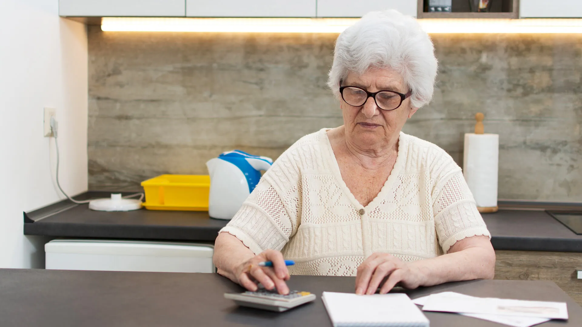 Elderly woman in kitchen calculating a budget