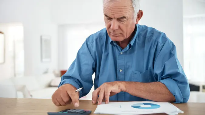 An retired man sits at his desk and does calculations.