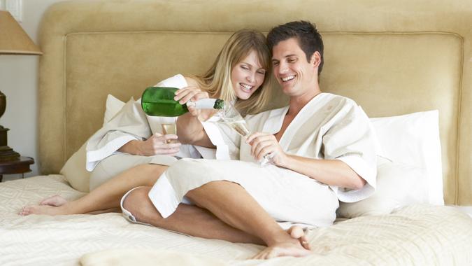 Free Hotel Upgrades That You're Missing Out On, Young Couple Enjoying Champagne In Bedroom, fees, America, money, payment, avoid fees, bills, debt