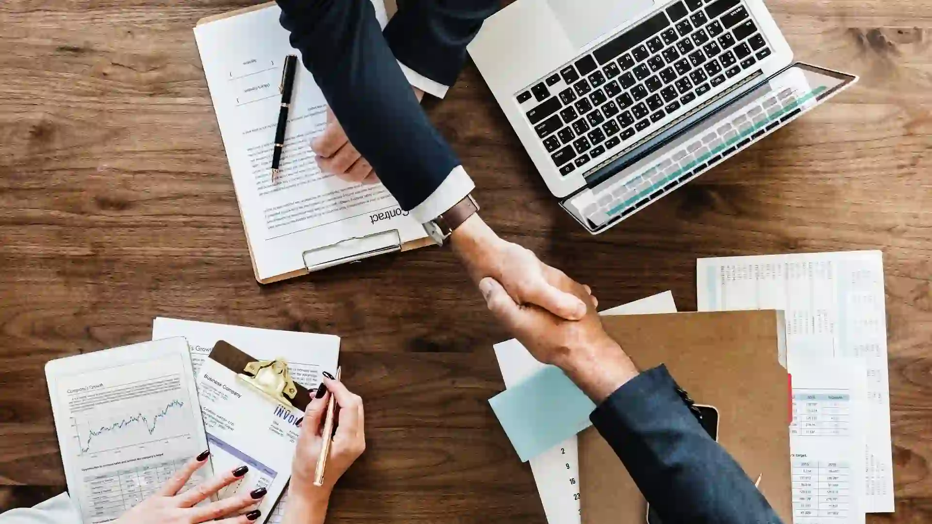 Businesspeople shake hands over contract papers.
