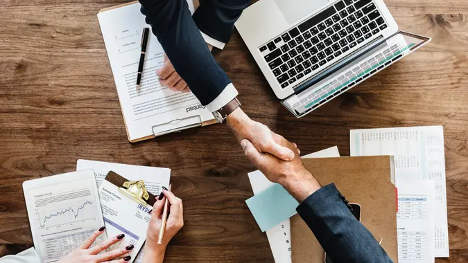 Businesspeople shake hands over contract papers.