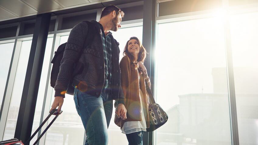 Shot of a young couple walking in anairport with their luggage while holding hands and looking at each other.