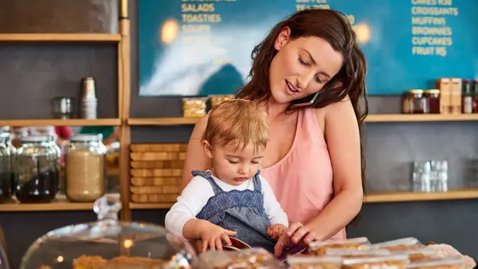 Shot of a woman talking on the phone in a bakery with her little girl next to her on the counter.