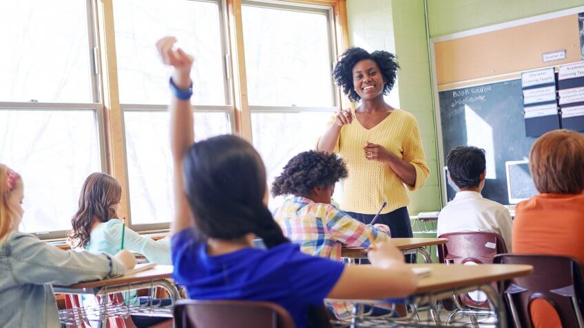 Shot of a young girl raising her hand to answer her teacher's question.