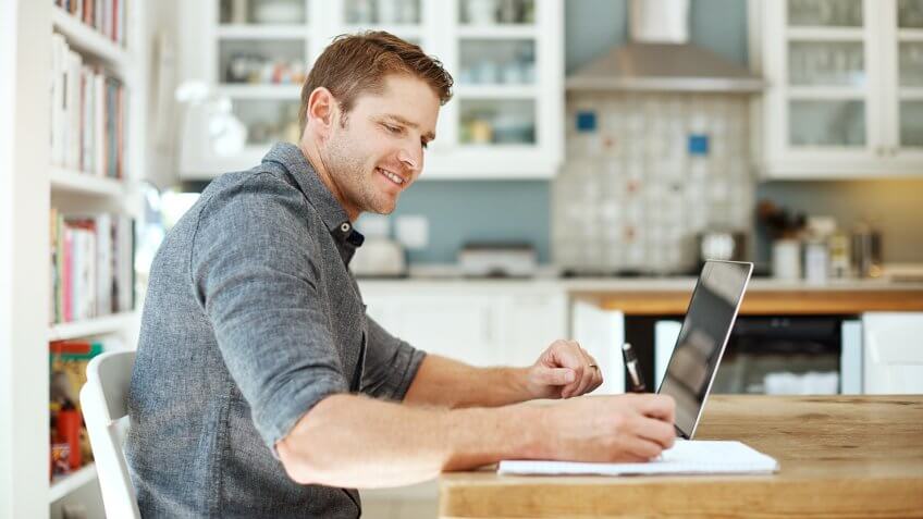 Shot of a young man using a laptop and writing notes at home. Shot of a young man using a laptop and writing notes at home.