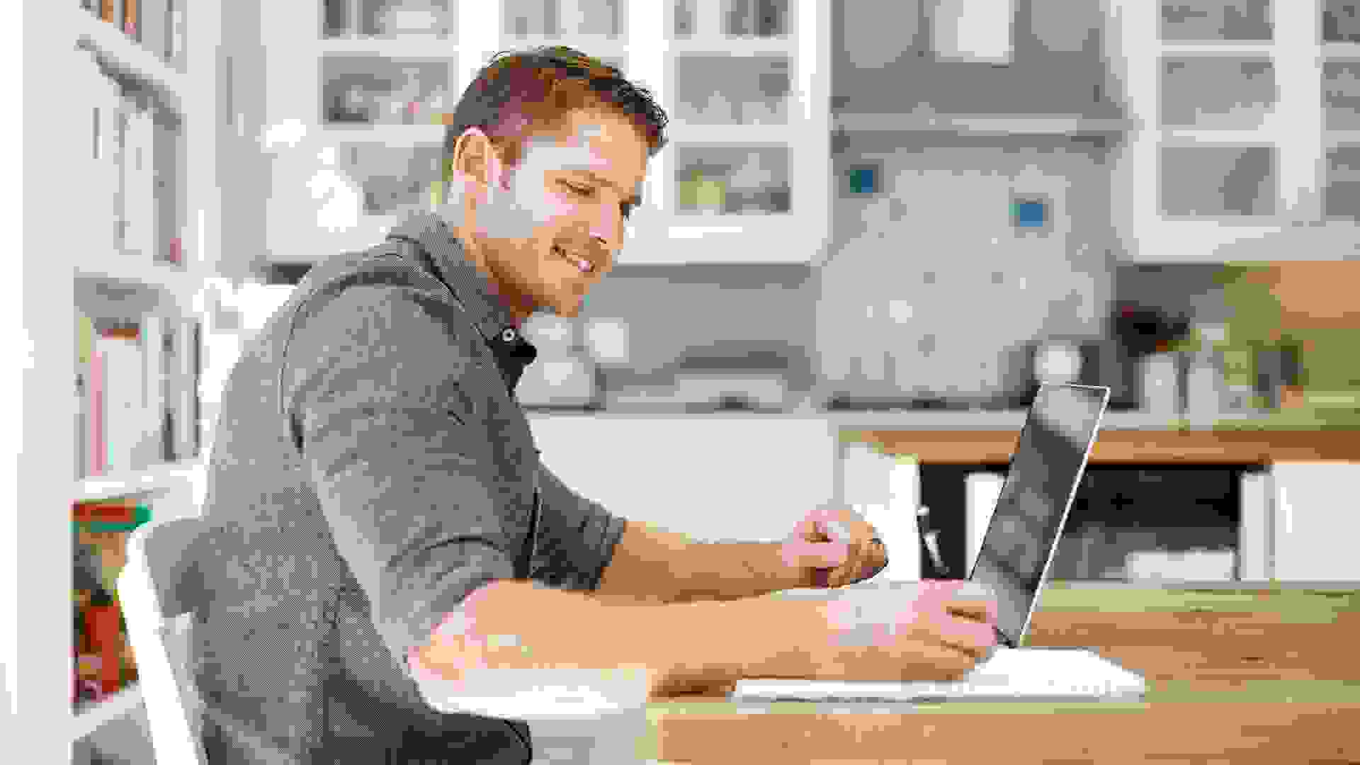 Shot of a young man using a laptop and writing notes at home.