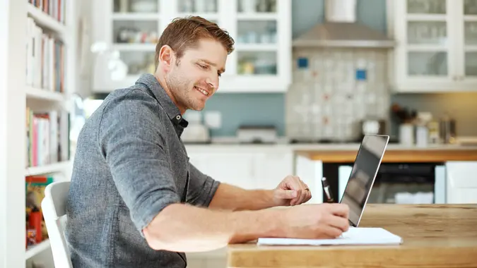 A man smiles as he works on his laptop.