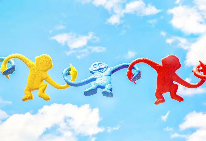 Yellow, blue and red plastic monkeys holding their hands against a blue sky.