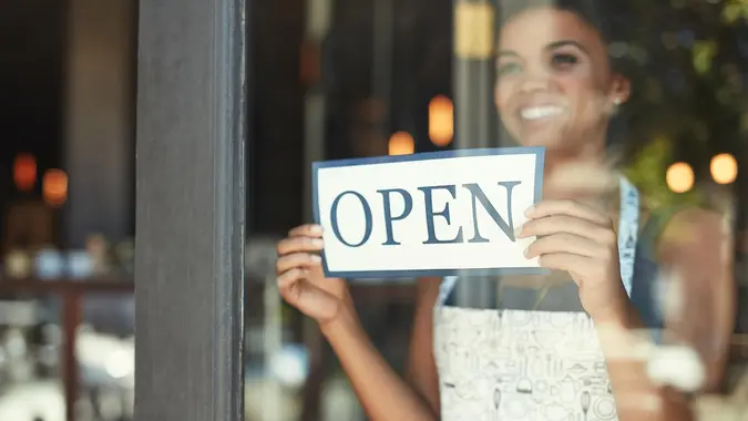 Young woman hanging up an open sign on the window of her cafe.