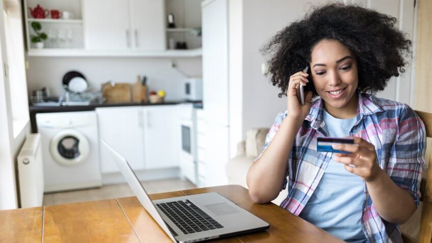 woman using credit card and talking on smart phone at home