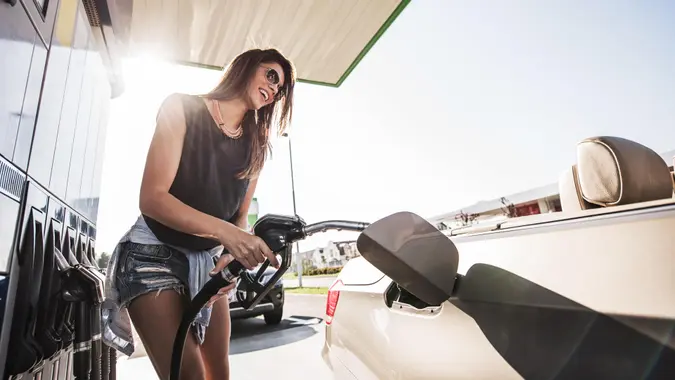 Below view of a young smiling woman refueling gas tank at fuel pump.