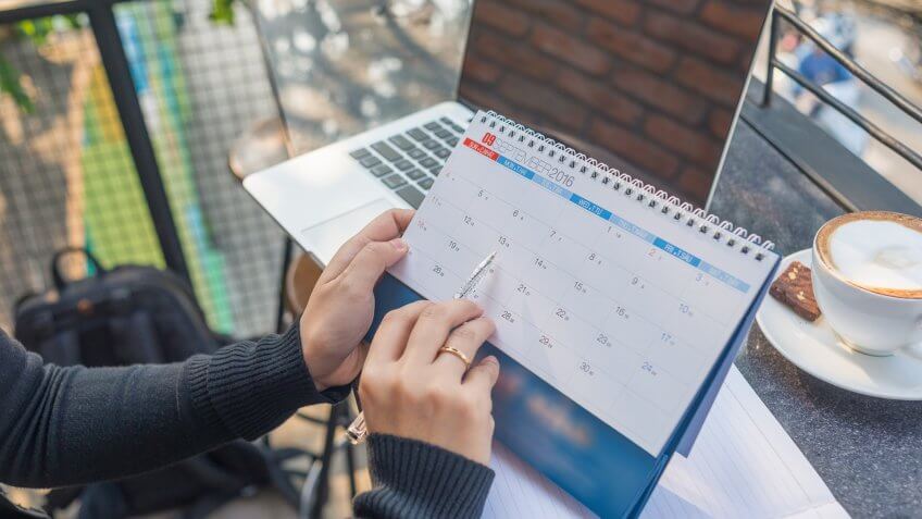 Woman’s hand carrying calendar and pointing on it by pen.