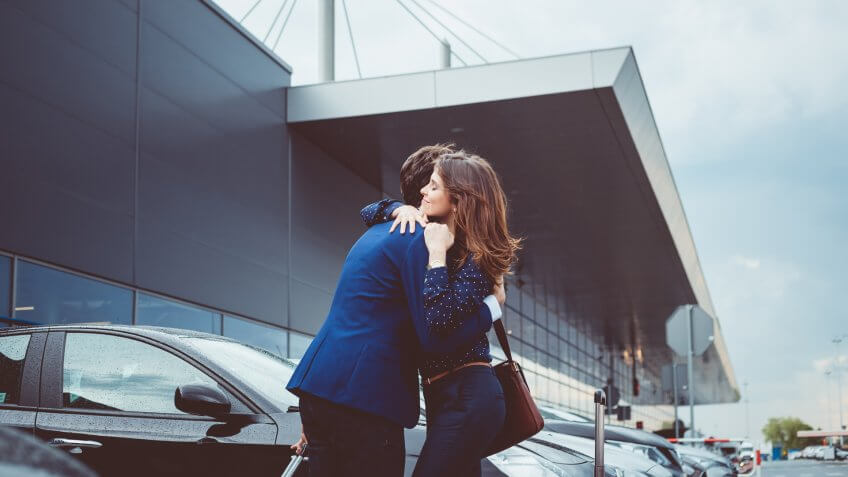 Young couple say good bye at airport, man and woman hugging each other at car parking lot.