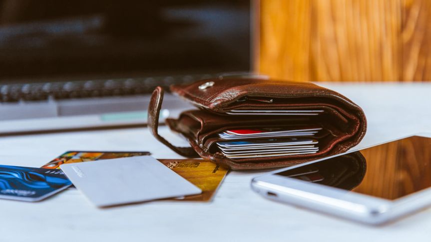 Wallet stuffed with credit cards sitting on a desk with a smartphone and laptop in the background