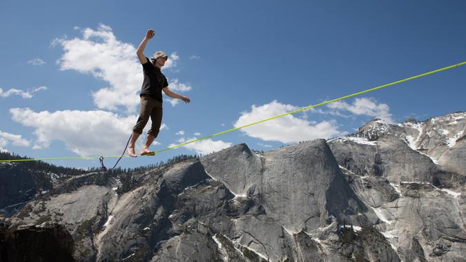 A male highliner walks across a one inch wide slackline in bare feet while highlining
