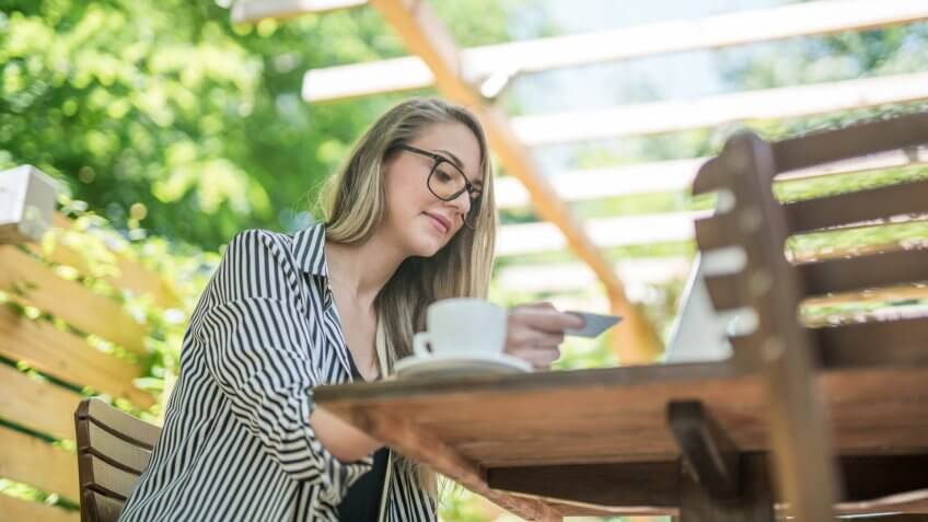 Young woman sitting in the cafe and paying bills and shopping with her laptop and paying by credit card.