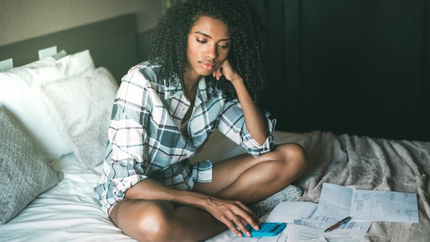 worried black woman with bills and finance problems on bed.
