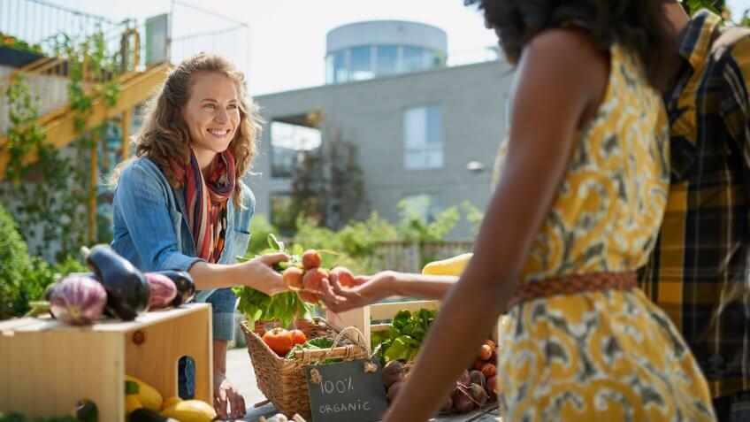 Female gardener selling organic crops and picking up a bountiful basket full of fresh produce