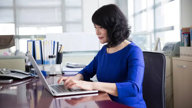 Woman in blue dress using laptop in office