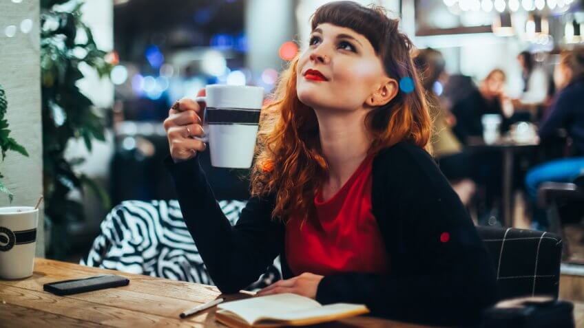 Woman Writing Journal at Window Seat in Coffee Shop.