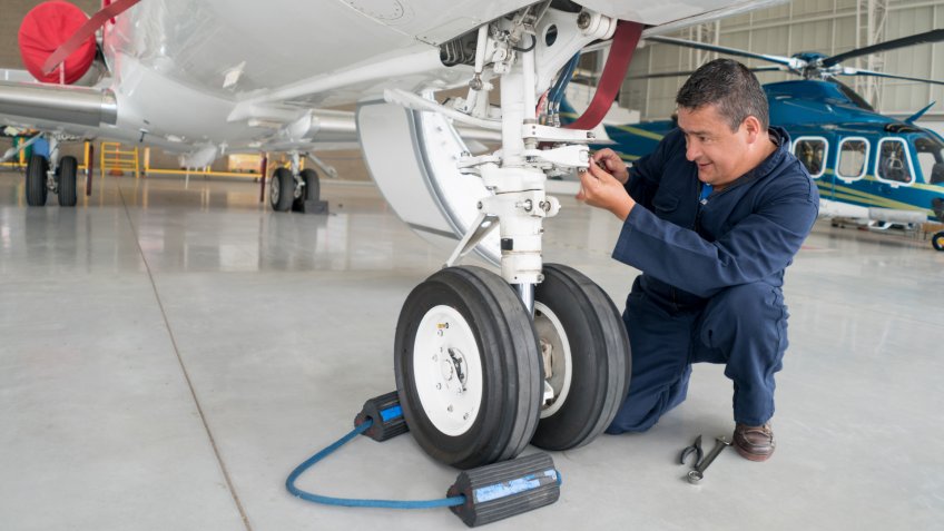 Happy mechanic working at an airplane hangar and fixing the landing gear of a plane.