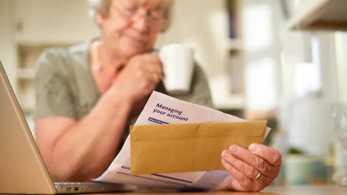 Senior woman looking at a bank statement at her laptop in the kitchen.