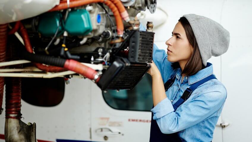 Young woman in uniform fixing something in air jet motor.