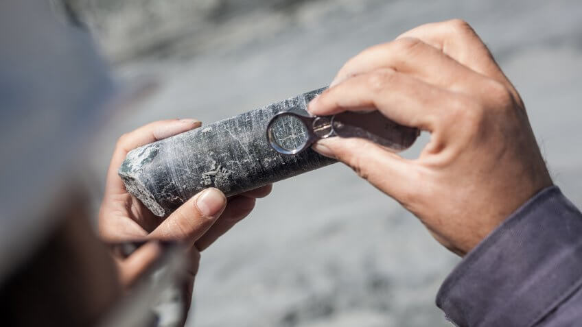 Engineer examining ore specimens with magnifying glass.