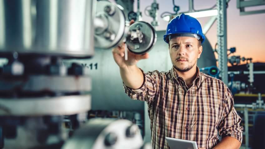 Man wearing blue hardhat using tablet at Natural gas processing facility.
