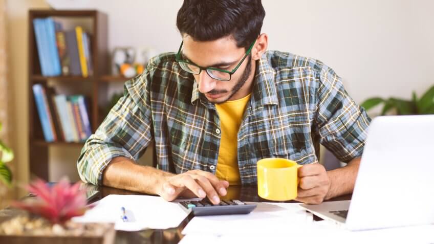 Man using calculator to calculate financial bills in home office.