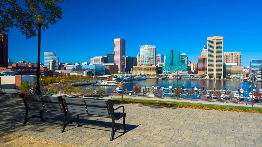 Downtown Baltimore with Inner Harbor view from Federal Hill Park, with a bench, lamp post, and tree.