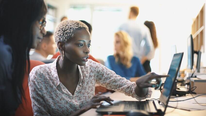 Closeup side view of two mid 20's black women doing their design project on a computer.