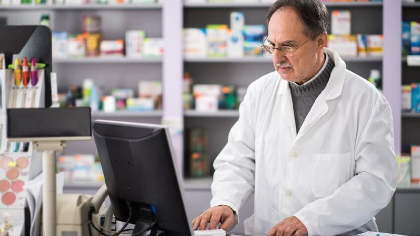 Senior pharmacist using desktop PC while working in a pharmacy.