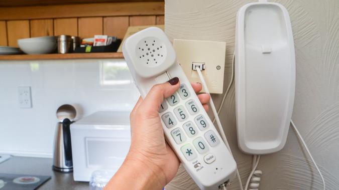 close up woman hold landline telephone at the house wall.