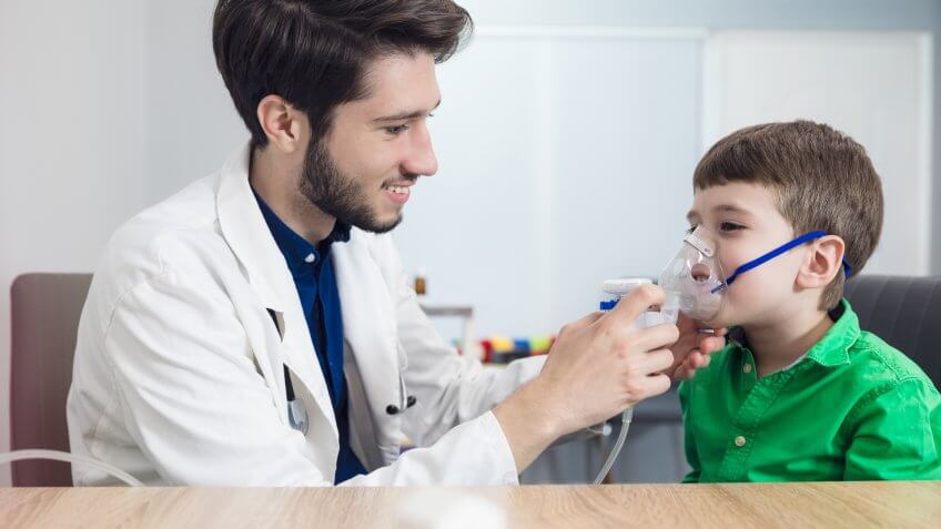 Respiratory Therapy technician holding inhaler mask for kid breathing in pediatrician clinic