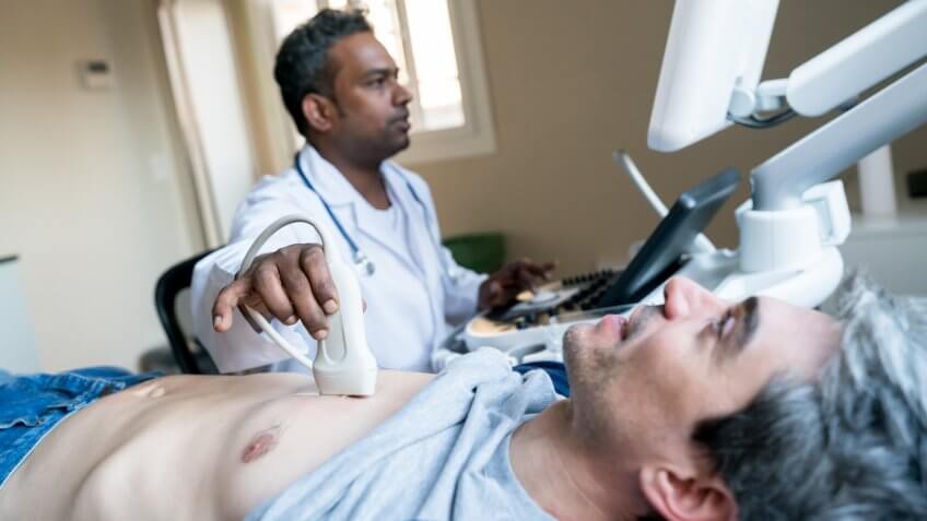 Cardiovascular Technologist doing a heart ultrasound to a middle aged male patient at the hospital.