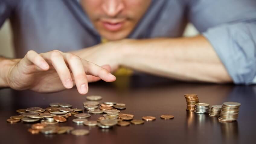 A man counts his coins on a tabletop.