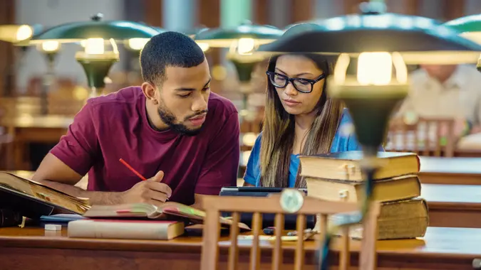 African american College student and asian girl using a digital tablet for doing research in the lecture room.