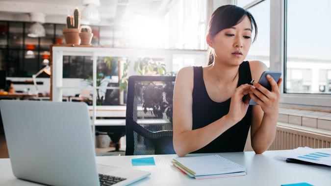 woman sitting at her desk with laptop and adhesive notes using mobile phone.