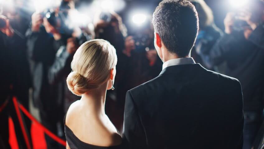 Celebrities posing for paparazzi on red carpet.