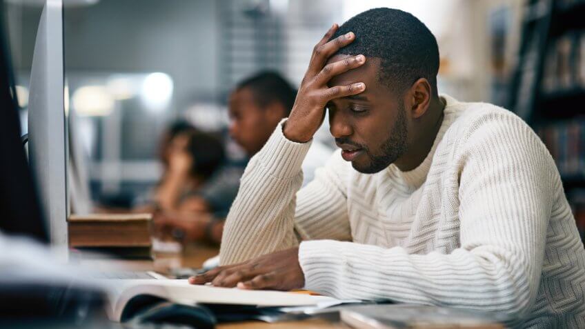 Shot of a young man studying in a college library and looking stressed.