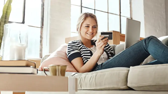 Shot of a young woman relaxing on the sofa and using a credit card with a laptop.